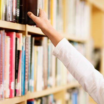 photo of a hand reaching for a book on the shelf