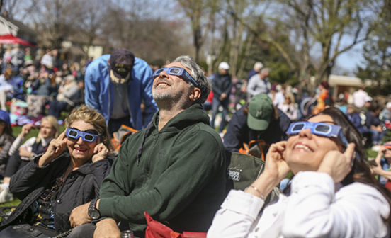 People in the park wearing eclipse glasses looking at the sky.