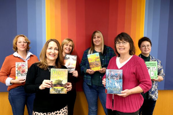 Info Advisors standing in front of rainbow painting holding their favorite books of 2025