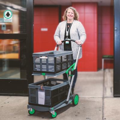 A volunteer carrying materials for home delivery to her car with a cart.